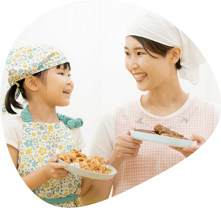 エプロン姿の大人と子どもが料理を手にして笑顔で向き合う場面